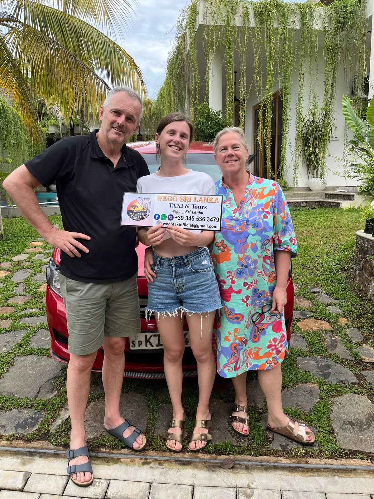 Happy family group with driver after completed tour Sri Lanka - International tourists holding Wego Taxi Tours sign celebrating successful vacation with guide